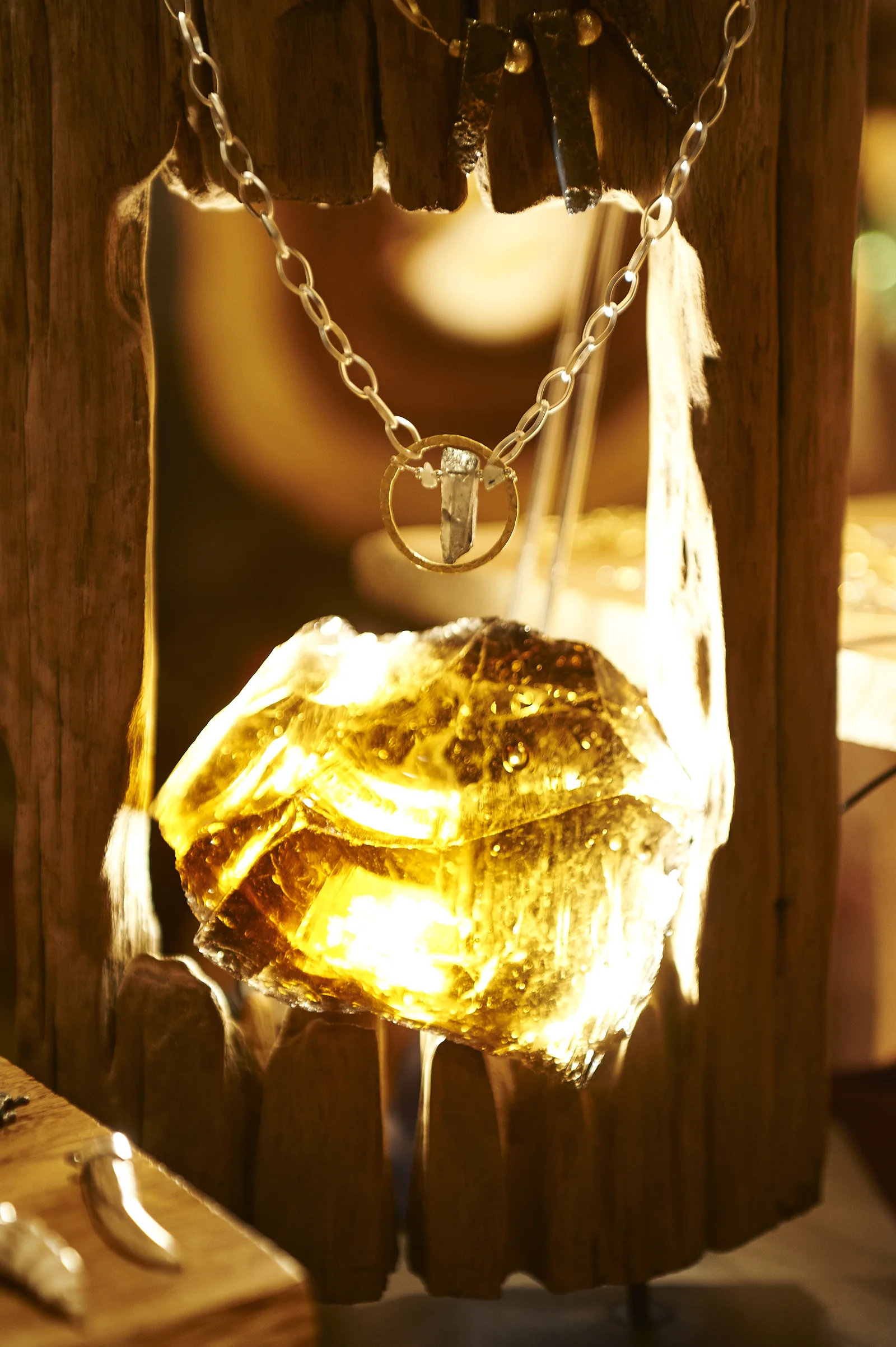 Halskette mit ringförmigem Anhänger vor einem beleuchteten Holzdisplay.